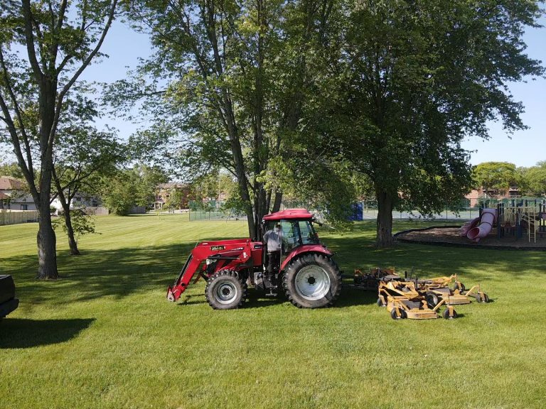 A red tractor rests on a grassy area beside a playground, where trees and a building frame the scene. This idyllic setting is perfect for showcasing Homewood irrigation system management expertise.